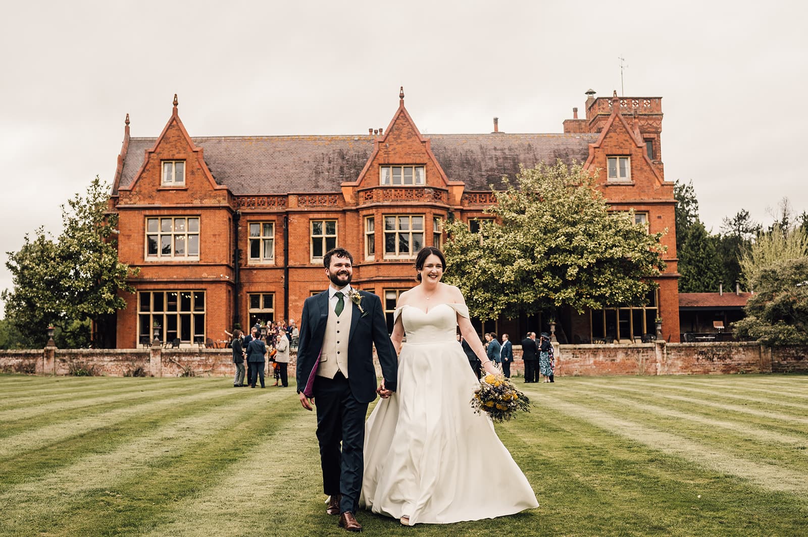 Bride and Groom walk the grounds of Holmewood Hall with the view of the wedding venue building in the background